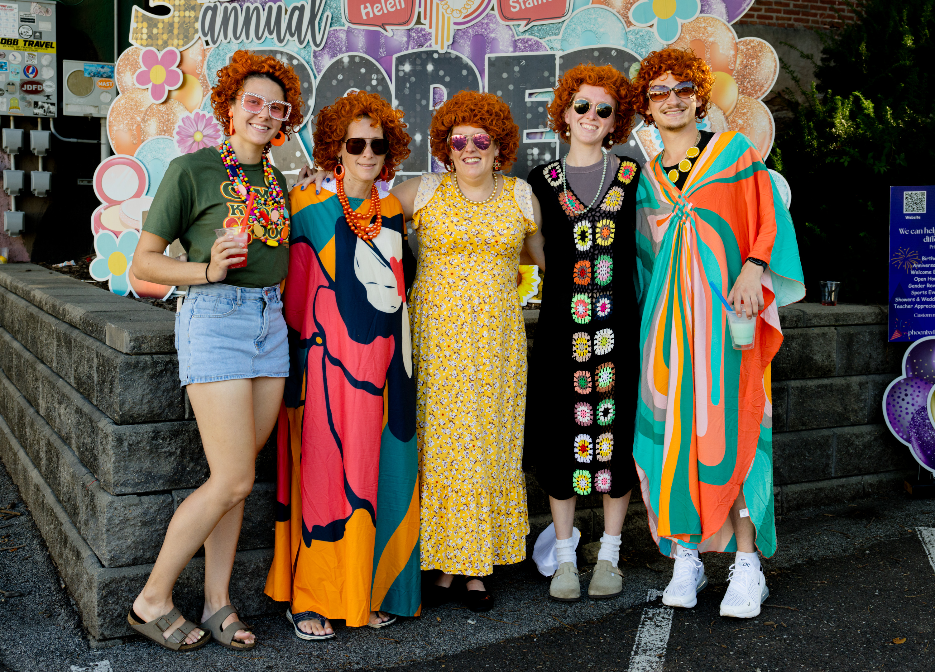 Five smiling Roper Romp participants wearing colorful caftans and orange wigs
