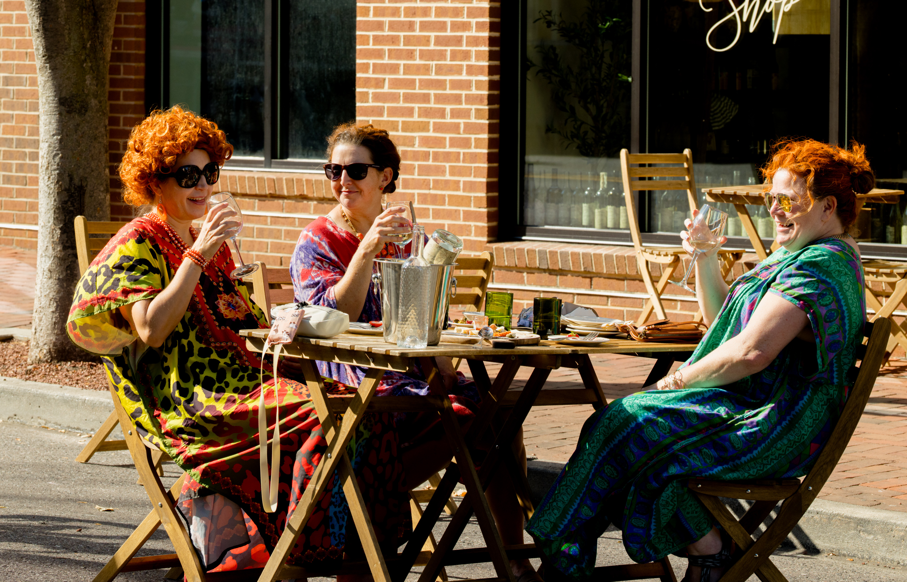 Three Roper Romp friends in colorful caftans enjoying drinks at a downtown table